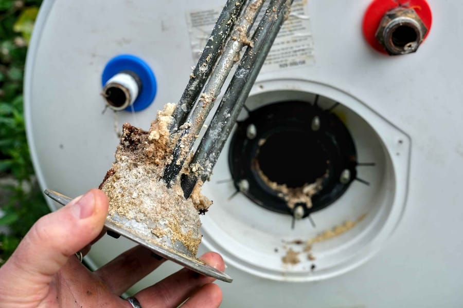 Electric water heater heating element, worn and covered with limescale. A hand is holding the heating element.