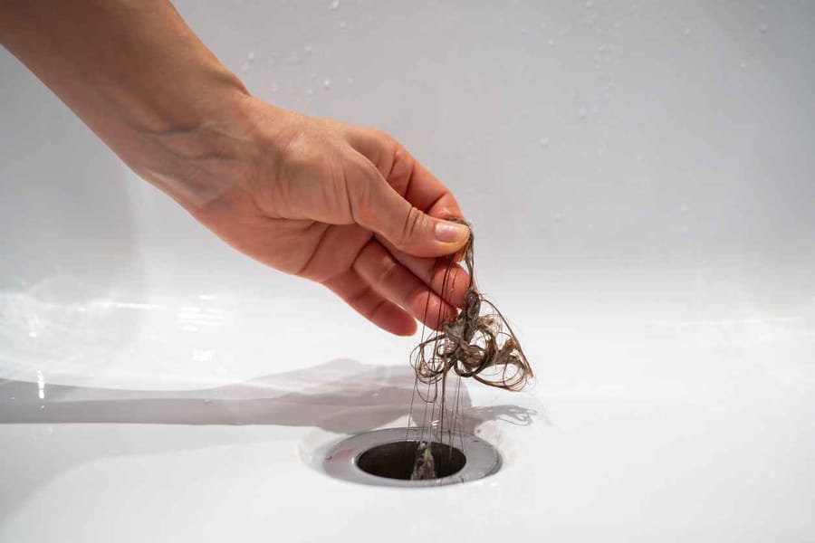 Hand pulls hair out of bathroom drain. Clump of hair being pulled out of bathroom drain
