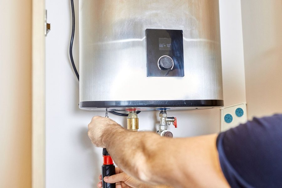 Technician tightening a valve on a stainless steel water heater for maintenance