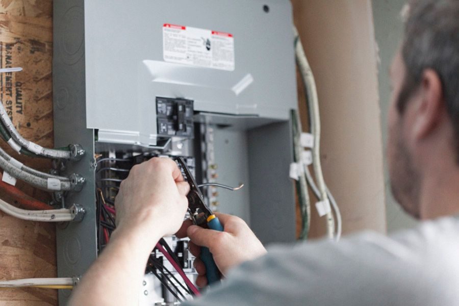 Technician wires a breaker panel, pulling and cutting wires inside an electrical service panel.