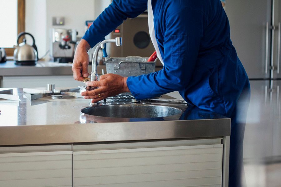 Person in a blue shirt repairing a kitchen faucet at an island counter.