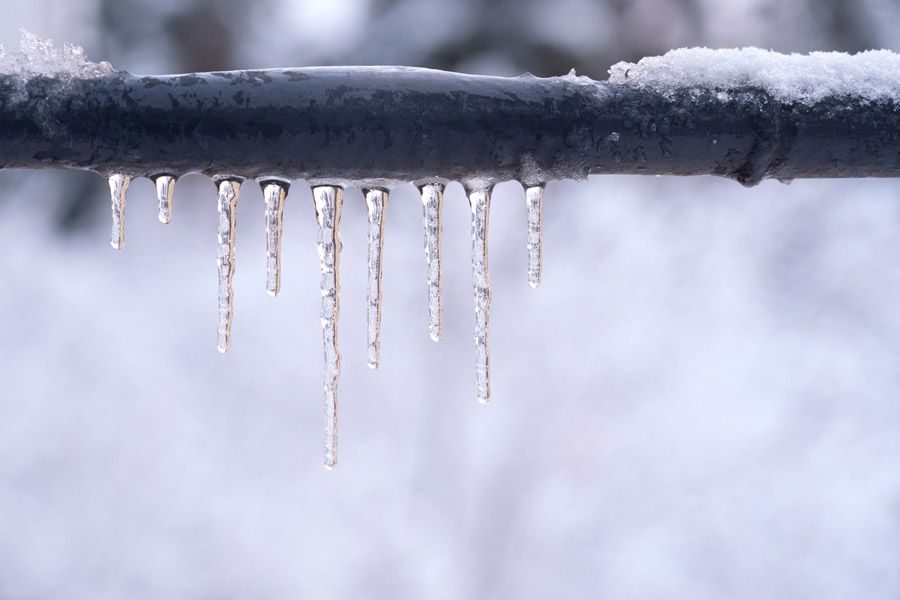 Icicles hang from a snow-dusted metal railing on a wintry day, with a blurred snowy background.