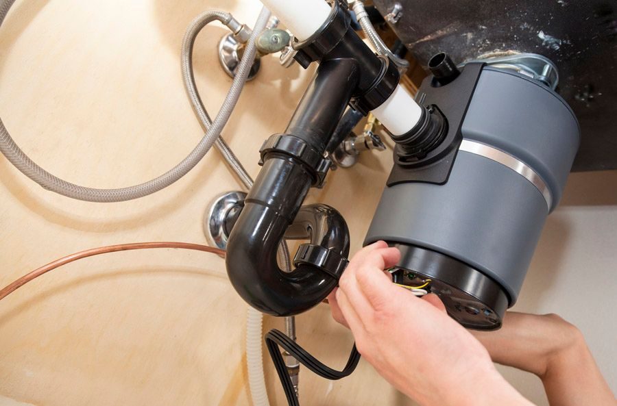 Person installs a garbage disposal under a kitchen sink, connecting the unit to the plumbing.