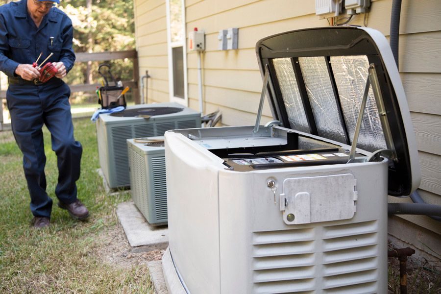 Technician in blue coveralls repairing an outdoor air conditioner with the service panel open beside the house.