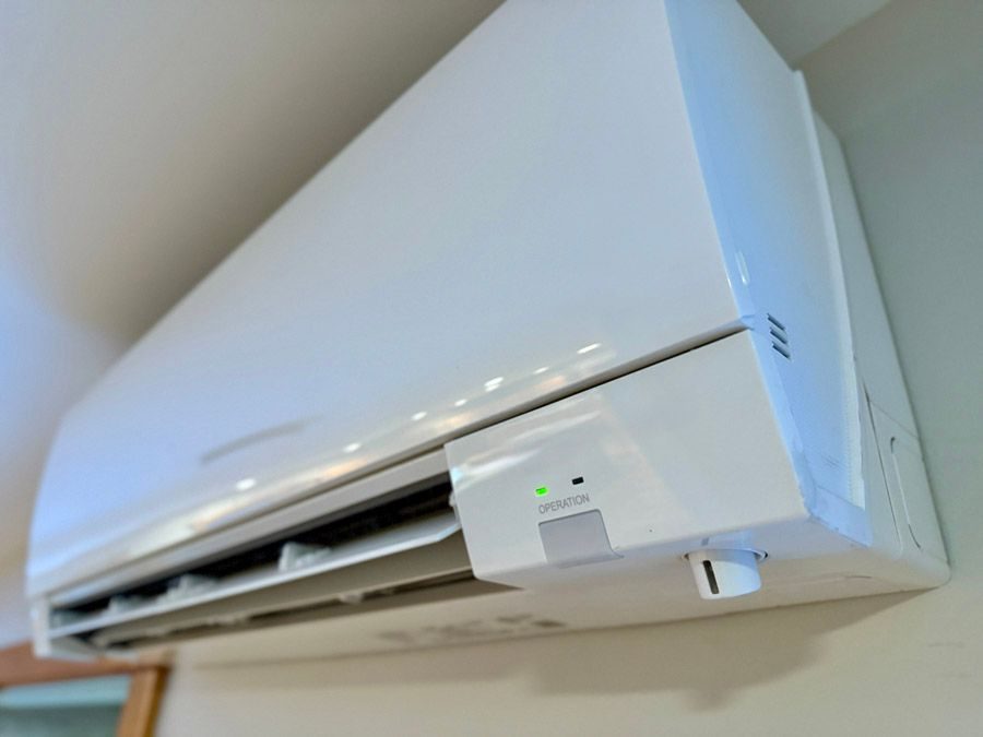 White wall-mounted air conditioner unit with vents open and a green operation indicator light on the front panel
