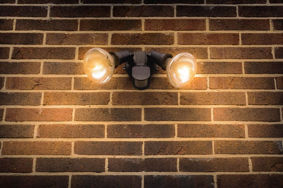 Dual outdoor wall light with two glowing bulbs mounted on a brick wall, wall-mounted fixture.