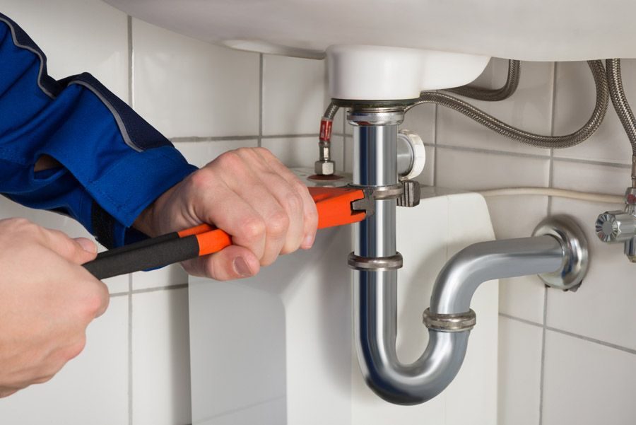 Hand using an orange-handled wrench to tighten the P-trap under a kitchen sink.