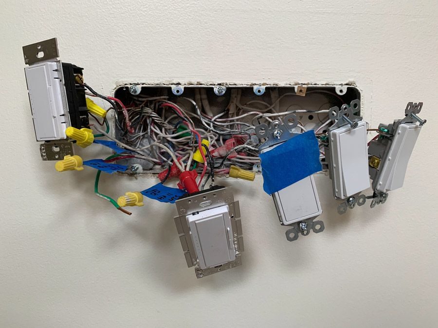 Open wall box with multiple light switches and a tangle of wires inside