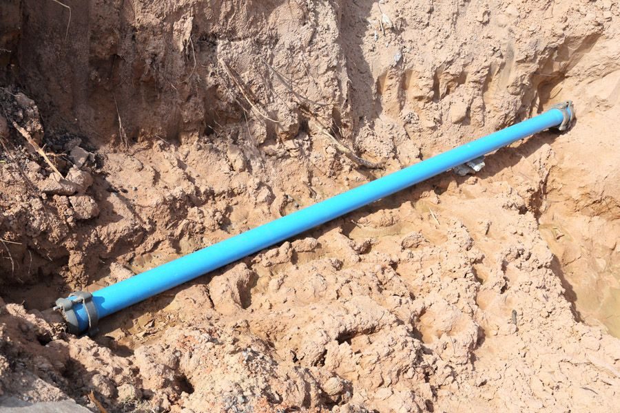 Blue PVC pipe laid in a dirt trench, with ends capped and connectors visible at both ends.