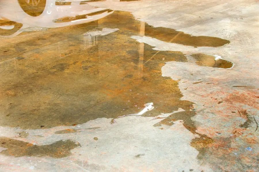Worn concrete floor with peeling paint and several brown water puddles.
