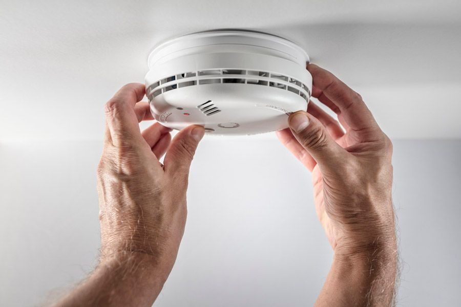 Hands mounting a white smoke detector to the ceiling (close-up)