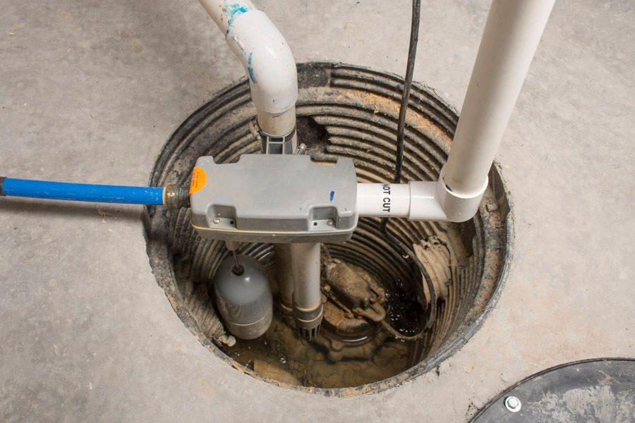 Open sewer cleanout in a concrete floor with connected PVC pipes and a repair/inspection device in the hole central to the image.