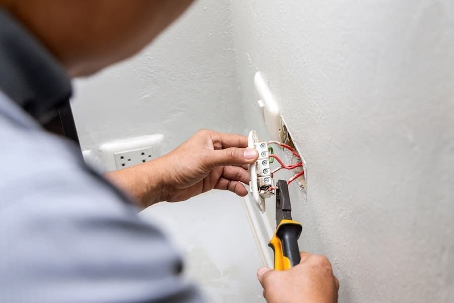 Person wires an electrical outlet, holding a cover plate and using pliers near a wall socket.