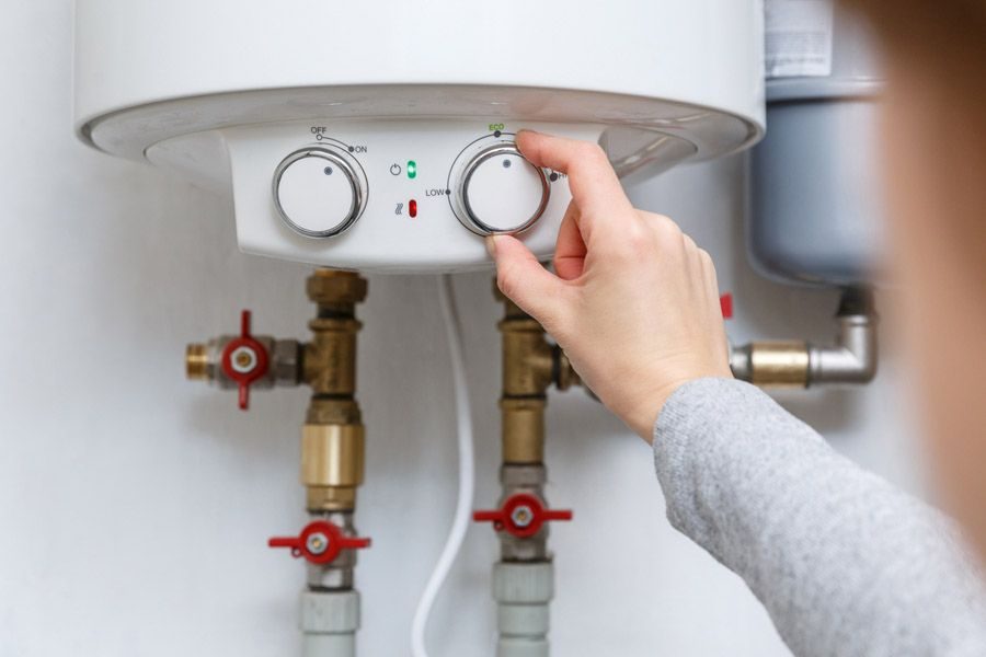 Person adjusting a white water heater knob labeled On/Off and Eco with red valve handles below the unit.