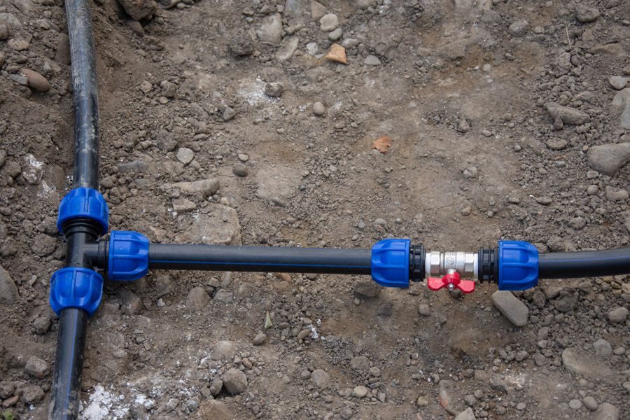 Underground irrigation/pipe line with blue compression fittings and a red shut-off valve in dirt.