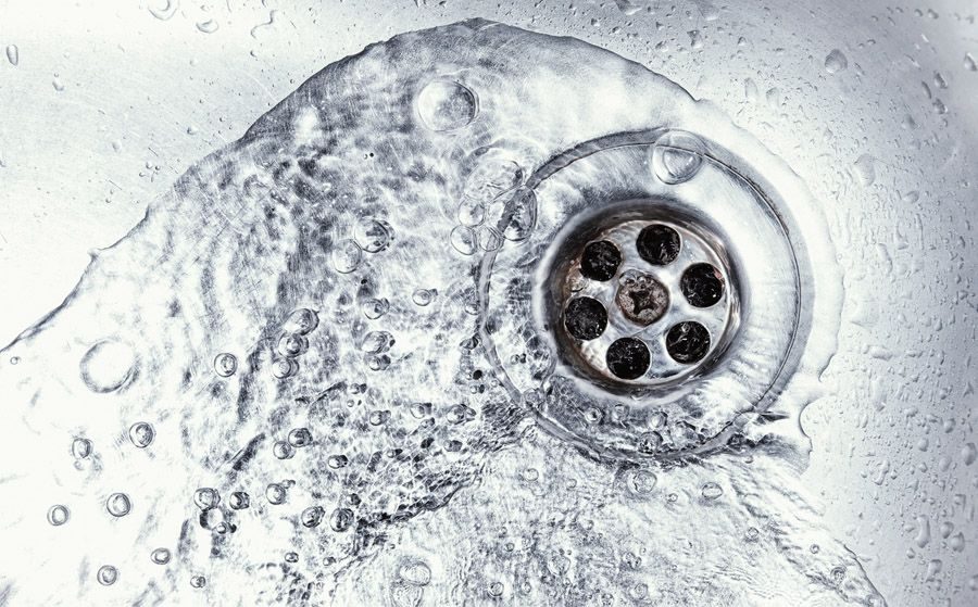 Close-up of a circular metal sink drain with water droplets and splashes around it.