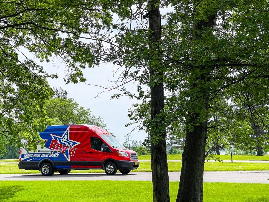 Red and blue service van with a star logo parked on a road beside a grassy park and leafy trees overhead.