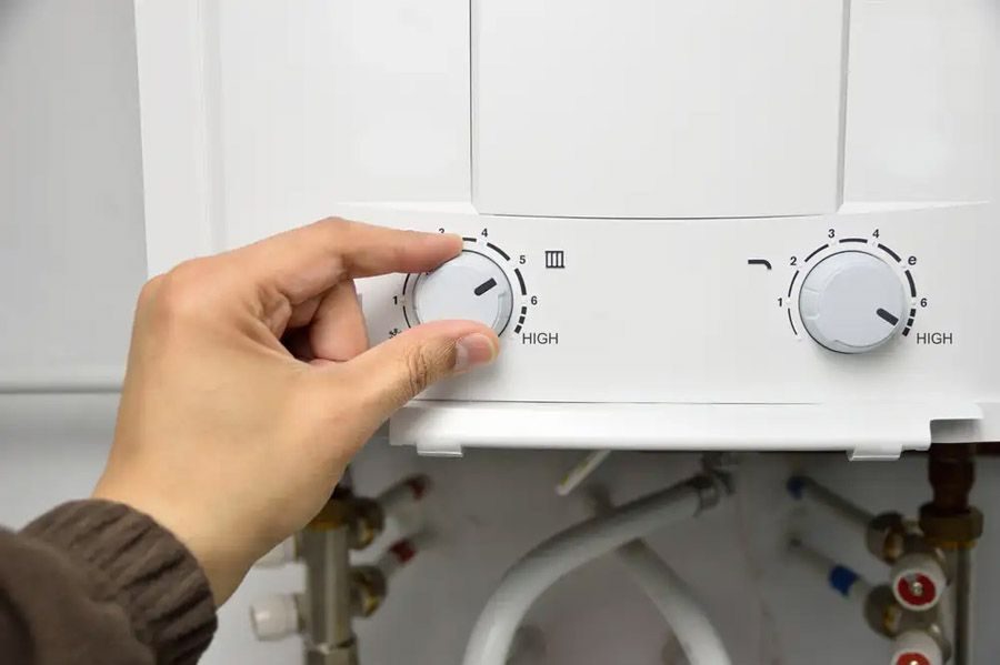 Close-up of a hand turning the left boiler knob on a white control panel with two dials labeled HIGH and numbered settings