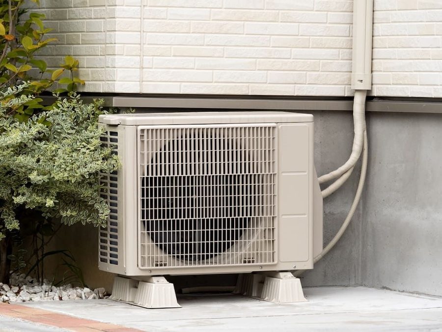 Heat pump outside of a home with a small bush nearby